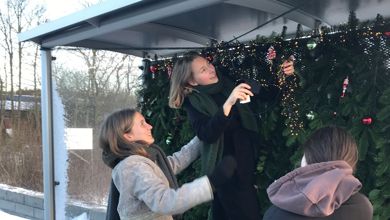 elever fra efterskole hænger julelys i busskur